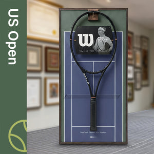 A ONE MAAY US Open-inspired blue hard court tennis racket wall display mounted elegantly next to a wooden bookshelf in a home library, featuring an olive-green side banner that reads "US Open"