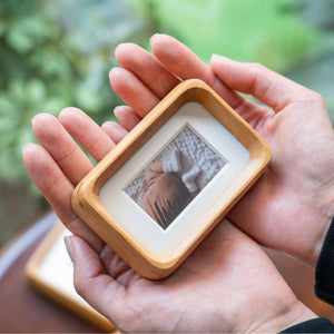 Person with hand holding a small teak wooden picture frame with a photo of a baby on a blurred green background