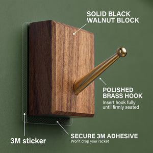 Detailed view of the solid black walnut block and polished brass hook with secure 3M adhesive used for mounting the racket on the ONE MAAY display